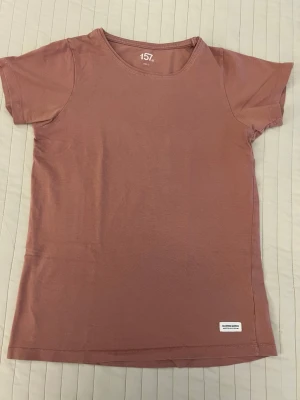 Brun t-shirt från 157 - Säljer en enkel brun t-shirt från 157 i storlek 150 cl. T-shirten har rund hals, korta ärmar och är gjord i mjuk bomull. Perfekt för dig som gillar basic och stilrena plagg. Liten vit etikett nere vid fållen.