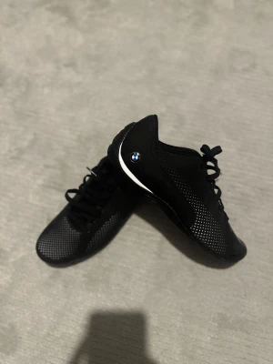 Svarta Puma BMW Motorsport sneakers - Säljer ett par svarta Puma BMW Motorsport sneakers med vitprickigt mönster på sidan, BMW-logga på hälen och Motorsport-tryck. Skorna har snörning, rund tå och platt sula. Materialet är syntet med ventilerande detaljer. Perfekt för dig som gillar motorsport och stil. Skorna är även aldrig använda se till och vara den första😀