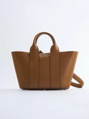 STYV BÄRVÄSKA - Snygg brun handväska i skinn med stilren design och rundade handtag. Väskan har en bred form och en praktisk axelrem som gör den enkel att bära. 