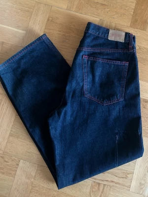 Mörkblå jeans från Weekday - Säljer ett par mörkblå jeans från Weekday med kontrasterande röda sömmar. Klassisk femficksmodell i loose passform och tillverkade i slitstarkt jeanstyg. Perfekta för dig som gillar en enkel men ändå unik look.