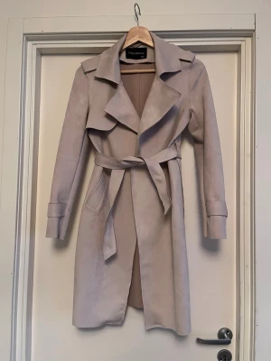 Beige trenchcoat  - Elegant trenchcoat i mjuk och skön borstad mocka. Storlek XXS men passar XS-S också. Ljus beige. Mycket bra skick! Upplagd på flera säljsidor, först till kvarn. 