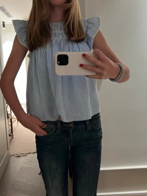 Randig blus från Polo Ralph Lauren - Säljer en söt blus från Polo Ralph Lauren i storlek 14 år (xs). Blusen är vit och ljusblå med smala ränder, har volangdetaljer vid axlarna och är ärmlös. Tillverkad i bomull. Rund hals och avslappnad passform. Endast använd fåtal gånger, skulle säga i nytt skick. Ny pris 800 kr.