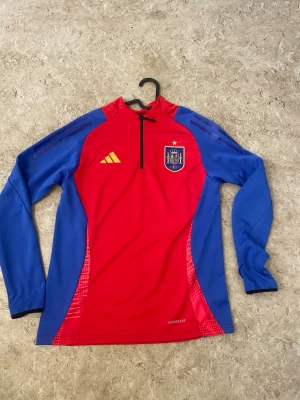 Ingen sko på bilden - Bilderna visar en långärmad träningströja från Adidas i rött och blått med Spaniens landslagsmärke, men ingen sko finns med.