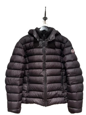 Svart pufferjacka från Colmar  - Säljer en svart pufferjacka från Colmar med huva och dragkedja framtill. Jackan har en quiltad design, två fickor med dragkedja och en logotyp på ärmen. Perfekt för kalla dagar när du vill hålla dig varm och snygg. Jackans luva går även att ta av. Vid mer frågor, hör av dig!