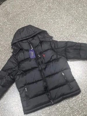 Svart pufferjacka från Polo Ralph Lauren - Svart pufferjacka från Polo Ralph Lauren med avtagbar huva, flera dragkedjefickor och ikonisk röd logga på bröstet. Jackan har quiltad design och är tillverkad i polyester, perfekt för kalla dagar. Snygg och praktisk med normal passform.