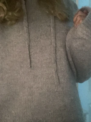 Stickad tröja - Storlek S. Mjuk och bekväm tröja i grå/beige färg med huva och snören. Avslappnad passform, ribbade kanter. I fint skick, använd en eller två gånger. Perfekt till vardags eller att bara ha hemma. 