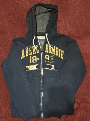 Abercrombie & Fitch Hoodie  - Snygg och bekväm zip-hoodie från Abercrombie & Fitch i mörkblå färg. Klassisk modell med snygga slitningar. Hoodien är i mycket bra skick och storleken är S men passar även M.