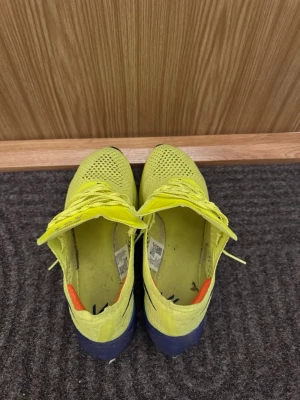Nike Vaporfly ZoomX löparskor gul - Nike Vaporfly ZoomX sneakers i en riktigt skarp gul färg med stickad mesh-överdel och snörning. Sulan är tjock och har en cool gradient från blått till orange. Swoosh-logga på sidan och Vaporfly-etikett på plösen. Perfekta för dig som gillar att springa snabbt och sticka ut.
