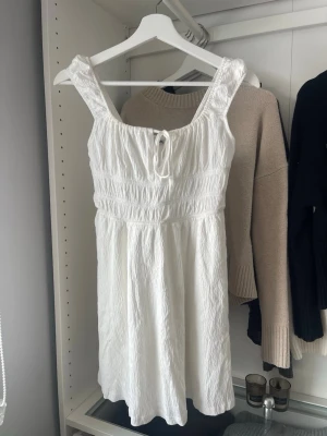 Vit kort sommarklänning - Söt kort klänning med breda axelband och knyt fram. Använd en gång, inga defekter tillkommer!💗