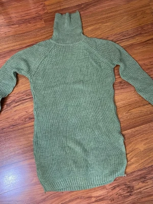 Olivgrön stickad polotröja - Säljer en olivgrön stickad polotröja i längre modell med ribbstickad struktur. Tröjan har långa ärmar och hög polokrage, perfekt för kyliga dagar. Materialet är mjukt och stretchigt, vilket gör den extra bekväm.