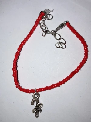 Rött pärlarmband med berlock - Snyggt armband med små röda pärlor och en silverfärgad berlock. Justerbart med kedja och karbinlås. Perfekt accessoar för att addera färg till din outfit.