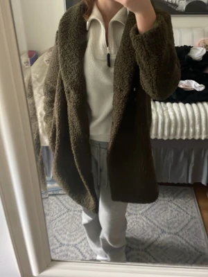 Mörkgrön teddyjacka med krage - Säljer en oversized mörkgrön teddyjacka med bred krage och mjukt, fluffigt material. Jackan har en avslappnad passform och går ner över höfterna. Skön till kyliga och vindiga dagar då den håller värmen.