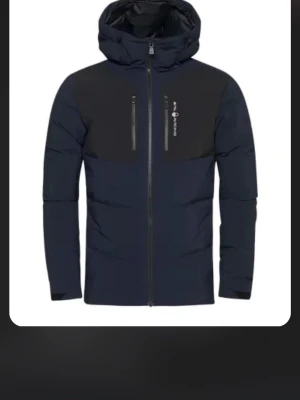 Dumont dunjacka dark navy - Snygg dunjacka i mörkblått från Dumont. Jackan har huva, dragkedja framtill och två bröstfickor med dragkedja. Färgblockad design med svarta axlar och ärmar samt mörkblå kropp. Perfekt för kalla vinterdagar. Storlek XXL