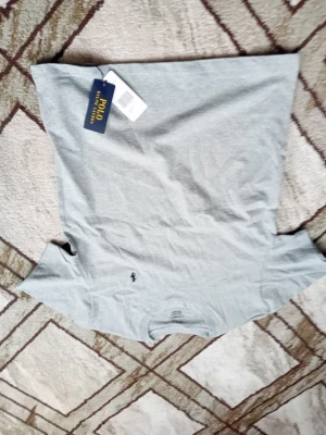 Grå t-shirt från Polo Ralph Lauren - Snygg grå t-shirt från Polo Ralph Lauren med klassisk rund hals och liten mörkblå logga broderad på bröstet. Tillverkad i mjuk bomull som känns skön mot huden. Perfekt basplagg till garderoben.