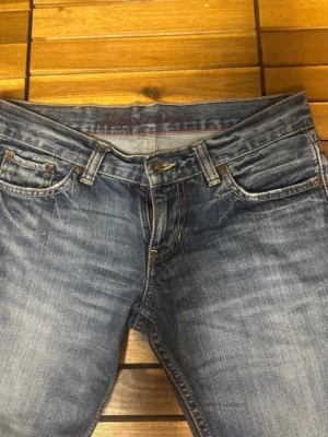 Blå Hilfiger Denim jeans - Säljer ett par klassiska blå jeans från Hilfiger Denim med snygga slitningar. Använder då de har blivit för små!