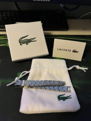 Lacoste armband - Mycket snyggt länkarmband från Lacoste. Helt nytt och aldrig använt. Går att ta av och på länkar. Skickar inom 24 timmar. Hör av dig vid frågor.