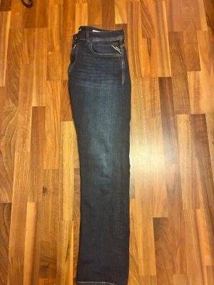 Mörkblå raka jeans från Replay - Snygga mörkblå jeans från Replay med raka ben och klassisk femficksmodell. Jeansen har kontrastsömmar och en diskret logga på bakfickan. Tillverkade i stretchigt denimtyg för extra komfort och passform. Storlek 33/32