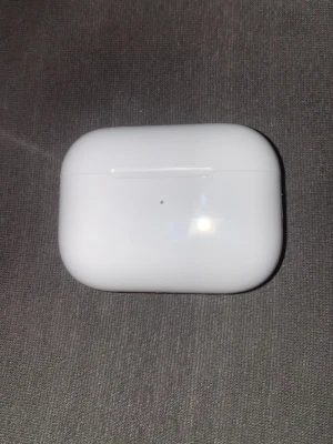 Apple AirPods Pro laddningsetui - Säljer ett vitt laddningsetui till Apple AirPods Pro. Etuiet har en stilren, blank finish och är tillverkat i plast. Kompakt och smidig design med magnetiskt lock och LED-indikator på framsidan. Perfekt för trådlös laddning och enkel förvaring av dina hörlurar.