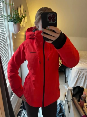 Röd/korall vindjacka från Everest med huva - Snygg röd vindjacka från Everest med svart dragkedja och detaljer. Jackan har huva, höga fickor med dragkedja och justerbara ärmslut. Perfekt för blåsiga dagar och outdoor-aktiviteter. Materialet är troligtvis syntet, vilket gör den lätt och smidig. Passar även 36 och 40. Ändats använd en dag.