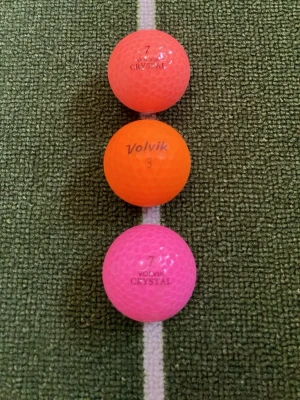 Färgglada golfbollar från Volvik - Tre golfbollar från Volvik i olika färger: en rosa, en orange och en röd. Bollarna har texten 'Volvik Crystal' och 'Volvik 3' tryckt på sig. Perfekta för dig som vill ha synliga golfbollar på banan.