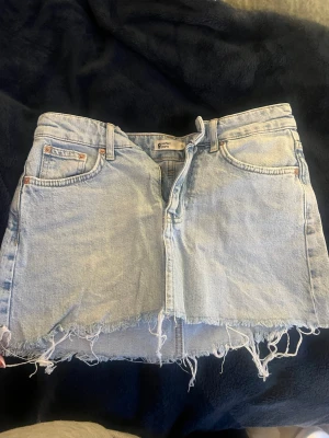 Ljusblå jeanskjol med fransig kant - Säljer en ljusblå jeanskjol från Perfect Jeans med rå, fransig kant nertill.