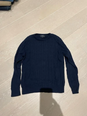 Mörkblå kabelstickad tröja Boomerang - Mörkblå kabelstickad tröja från Boomerang med rund halsringning och ribbade muddar. Klassisk och stilren design, perfekt för lager-på-lager. Tröjan är i mjukt material och har diskret struktur i stickningen.