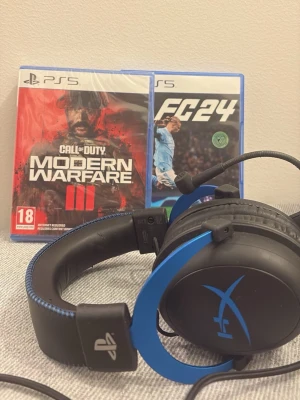 HyperX gaming headset + två ps5 spel - Säljer ett HyperX gaming headset i svart och blått med PlayStation-logga på sidan. Mjuka öronkuddar och vadderat huvudband i konstläder. Perfekt för gaming och passar till PS5. Slitstark design med tydlig HyperX-logga på bågen.