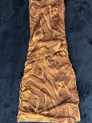 Kaffe mönstrad kortklänning - Säljer en kortklänning med brunt och beige marmorerat mönster. Storlek S. Klänningen har en åtsittande passform och är ärmlös. Materialet känns mjukt och stretchigt, vilket gör den bekväm att bära.