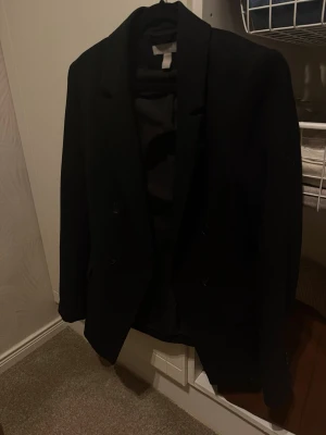 Svart kavaj med dubbelknäppning - Stilren svart kavaj med dubbelknäppning och klassisk krage. Slim fit