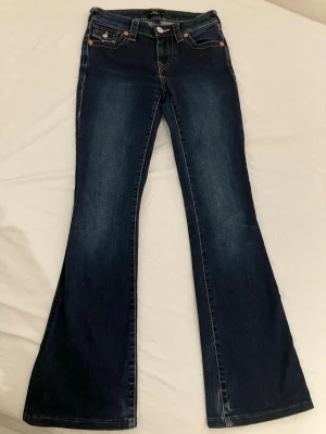 Bootcut jeans från True Religion Becca 24” - Mörkblå bootcut jeans Becca från True Religion med snygga kontrastsömmar och detaljerade bakfickor. Klassisk femficksmodell med orange sömmar och silverknapp. Tillverkade i slitstark denim som ger en cool vintagekänsla.