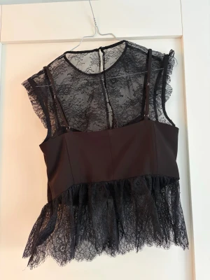 Svart spetsig korsettopp - Snygg svart korsettopp med transparent spets upptill och nertill. Toppen har smala axelband, markerade kupor och dragkedja i ryggen. Perfekt för att lyfta vilken outfit som helst med en edgy vibe.