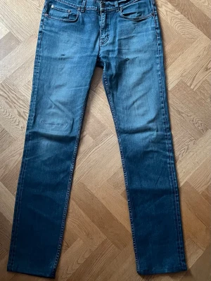 Blå slim fit jeans från Acne Studios - Snygga blå slim fit jeans från Acne Studios med klassisk femficksdesign och subtila slitningar framtill. Jeansen har normal midja, dragkedjegylf och är tillverkade i mjuk denim med lätt stretch för skön passform.