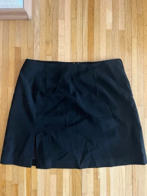 Svart minikjol från Djerf Avenue - Stilren svart minikjol från Djerf Avenue med rak passform och diskret slits framtill. Kjolen är helfodrad och har en klassisk look som passar till många olika outfits. Perfekt för dig som gillar minimalistisk och trendig stil. Nypris: 650kr