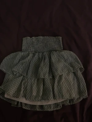 Grön volangkjol från Kappahl - Supersöt grön kjol från Kappahl med vågigt mönster och flera volanger. Kjolen har smock i midjan för en bekväm passform och är perfekt för dig som gillar en lekfull och trendig stil.