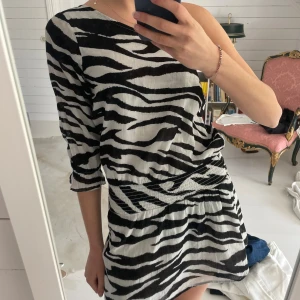 Zebramönstrad kortklänning Gina Tricot - Snygg kort klänning från Gina Tricot i samarbete med Izaandelle. Klänningen har svartvitt zebramönster, oneshoulder-design och trekvartsärm. Den är tillverkad i mjuk bomull och har en markerad midja som ger en cool siluett. Perfekt för dig som gillar att sticka ut. Jag har storlek XS och passar ändå i storleken