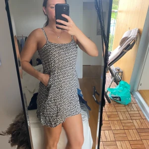 Svartvit kort klänning med mönster - Supersöt kort klänning med svartvitt geometriskt mönster och tunna axelband. Lätt och luftig modell som sitter skönt och har en avslappnad passform. Perfekt för varma dagar och enkel att styla med sneakers eller sandaler.