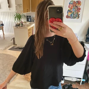 Svart blus med knyt i ryggen - Säljer en svart blus med vida trekvartsärmar och snygg knytning i ryggen. Blusen har en lös passform och är perfekt att styla med jeans eller kjol. Materialet känns lätt och luftigt, vilket gör den skön att bära hela dagen.