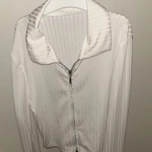 Vit ribbad ziptröja med krage - Snygg vit långärmad tröja med dragkedja framtill och bred krage. Tröjan har ribbat mönster som ger en stilren look och är perfekt för lager-på-lager. Passar dig som gillar minimalistisk och fräsch stil.