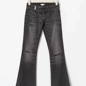 Svarta bootcut jeans med slitningar - Snygga svarta bootcut jeans med slitna detaljer på benen och markerade sömmar. Jeansen har stora framfickor och dubbla knappar i midjan. Perfekta för dig som gillar en edgy och trendig look.