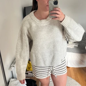 Vit stickad oversized tröja - Supermysig vit stickad tröja med bred ribbad struktur och rund hals. Tröjan har en oversized passform och långa ärmar, perfekt för lager-på-lager och chill dagar. Enkel att matcha med jeans eller leggings.