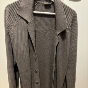 Grå stickad kofta från John Henric - Säljer en stilren grå stickad kofta från John Henric i storlek L. Koftan har klassisk krage, knäppning framtill med knappar och är långärmad. Perfekt för lager-på-lager och passar till många olika outfits.