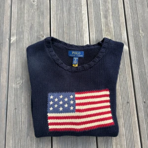 Mörkblå stickad tröja Polo Ralph Lauren - Säljer en mörkblå stickad tröja från Polo Ralph Lauren i storlek ung XL men sitter som herr S. Tröjan har ett broderat amerikanskt flaggmotiv på bröstet och RL-broderi nertill. Klassisk rund halsringning och långa ärmar. Perfekt för dig som gillar preppy stil!