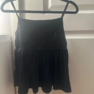 Svart paljettlinne från Gina Tricot - Svart linnetopp från Gina Tricot med tunna axelband och glittrig paljettöverdel. Strl 158/164 men passar XS-S