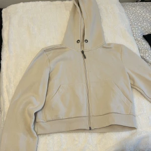 Beige hoodie från Page One XS - Snygg beige hoodie från Page One i storlek XS. Tröjan har dragkedja framtill, huva med metallöljetter och två fickor. Mjuk insida och ribbade muddar nedtill och vid ärmslut. Perfekt för en chill och avslappnad stil.