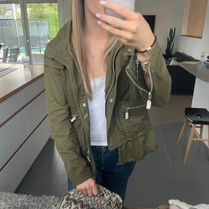 Grön Zara jacka!!! - Säljer min skitsnygga olivgröna Zara jacka med luva, dragkedjor på fickor och ärmslut samt snygg volangkant nedtill. Avslappnad passform, perfekt längd och både dragkedja och knappar. Använd men tvär bra skick💕💕