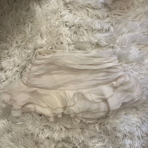 Ljusbeige volangkjol lågmidjad - Supersöt kort kjol i ljusbeige med volanger och omlott-design. Kjolen har ett skirt, lätt material som ger en flowy känsla och passar perfekt till sneakers eller boots. Perfekt för dig som gillar romantisk och feminin stil.