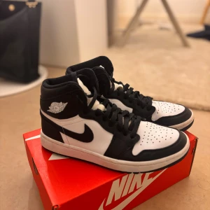 Nike Air Jordan 1 High svart/vit - Säljer ett par Nike Air Jordan 1 High i svart och vitt skinn. Helt nya använda en gång hemma. Klassisk siluett med svart swoosh, perforerad tå och högt skaft. Ikonisk Jordan-logga på sidan och svart snörning. Perfekta för dig som vill ha en clean och tidlös sneaker. Boxen finns ej med men de är helt äkta som kan identifieras med serialnummer och QR koden i skorna
