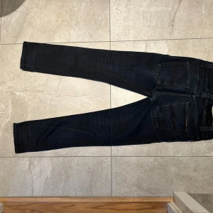 Svarta jeans från Nudie Jeans Co - Säljer ett par svarta jeans från Nudie Jeans. Jeansen har raka ben, snygga kontrastsömmar på bakfickorna och är tillverkade i slitstark denim. Perfekta för dig som gillar stilrena och tidlösa jeans.