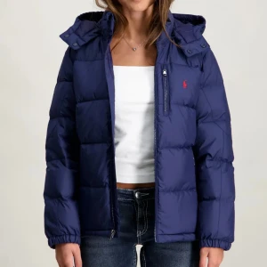 Mörkblå pufferjacka från Polo Ralph Lauren - Säljer en mörkblå pufferjacka från Polo Ralph Lauren i storlek XL (Junior) är som S i Dam Storlek. Jackan har huva, dragkedja framtill, flera fickor med dragkedja och den klassiska röda Polo-loggan på bröstet. Perfekt för kalla dagar och riktigt snygg till jeans eller sweatpants. Nypris 3295 kr men väljer att sälja för 2000 då den är som ny!