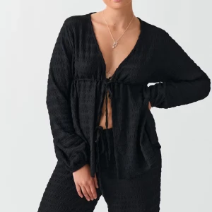 Svart blus GinaTricot - Svart knyt blus från Gina Tricot i strukturtyg. Blusen har långa ärmar, knytning framtill och en lös, flowy passform så den passar även som S. Slutsåld på hemsidan.
